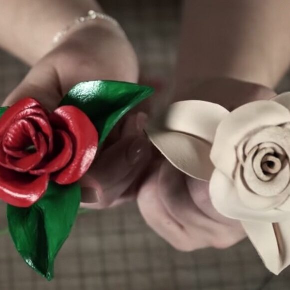 Пальцы бережно придерживают изящные кожаные изделия из кожи, созданные с невероятным мастерством. Первый цветок роза насыщенного алого оттенка, украшенный нежными зелеными лепестками, привлекает внимание своей яркостью.